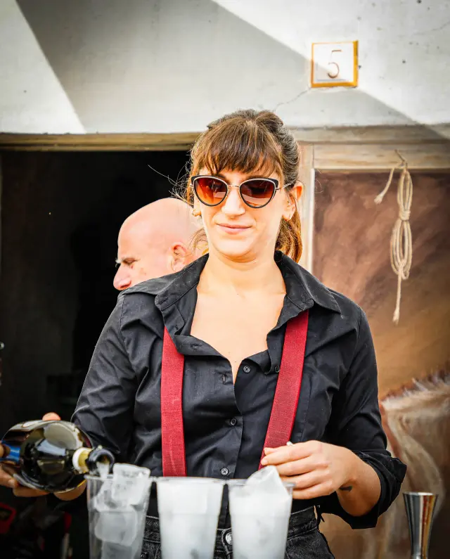 Bartender con bretelle rosse che versa un cocktail al banco bar