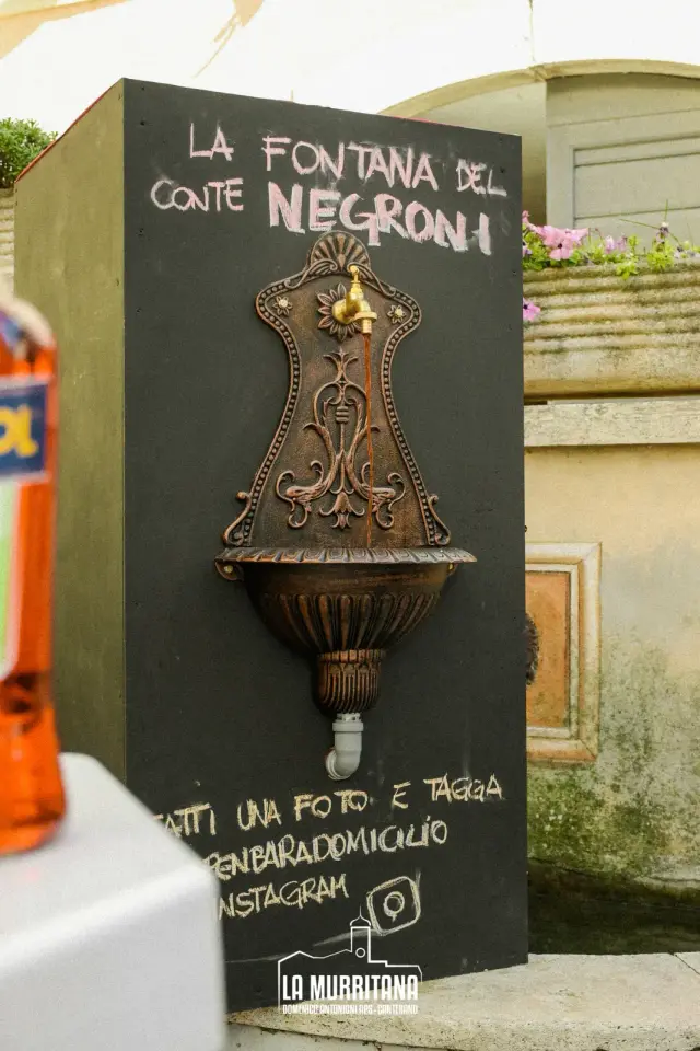 Cartello "La Fontana del Conte Negroni" con vecchia fontana in ferro battuto, allestimento La Murritana
