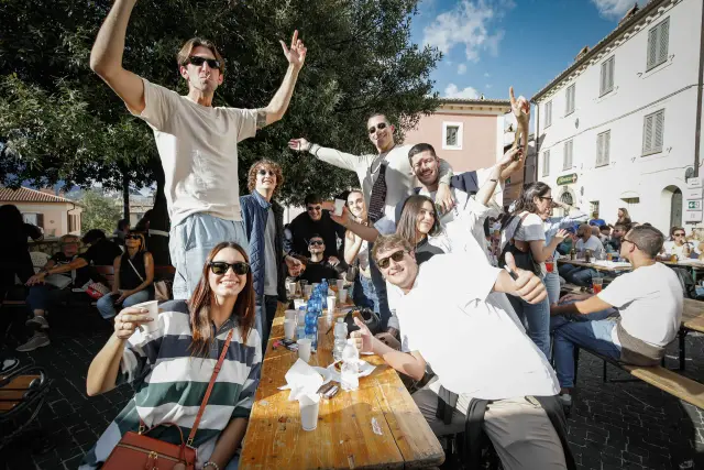 Gruppo di amici sorridenti con le braccia alzate a un tavolo della sagra