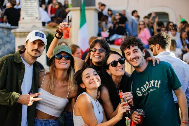 Gruppo di amici con drink in mano davanti al monumento e alla bandiera italiana