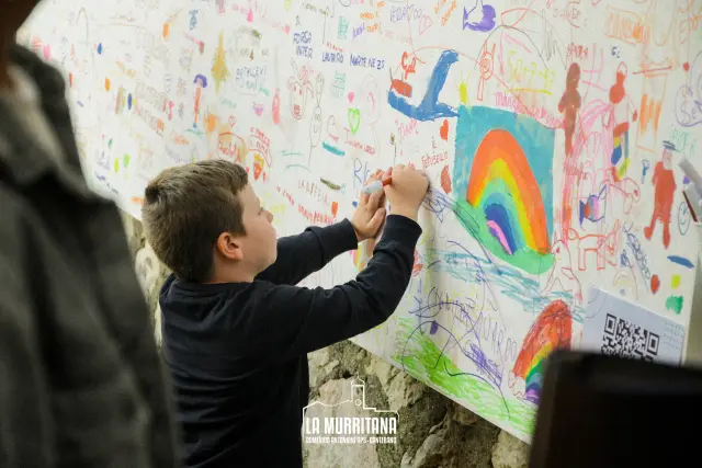Bambino che disegna su un grande murale di carta durante l'attività per bambini della sagra