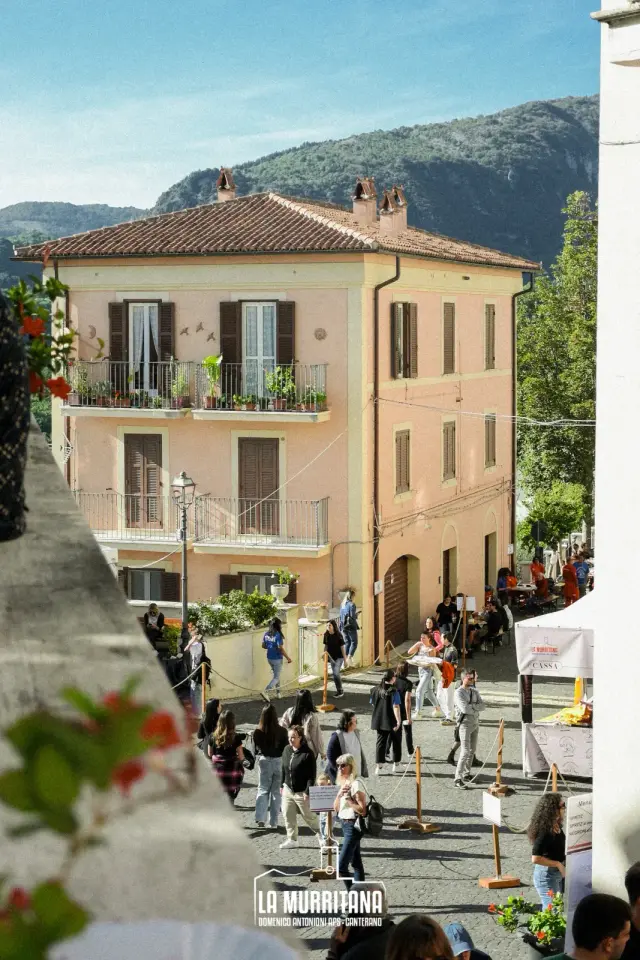 Palazzo storico color rosa antico con vista sulle montagne e visitatori nella piazza della sagra