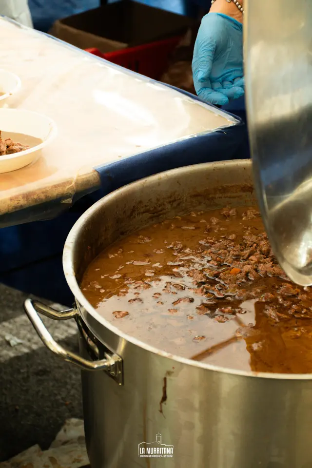 Grande pentola di sugo di carne mescolato durante la preparazione del ragù