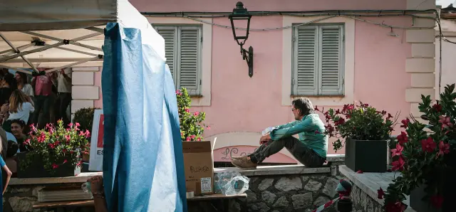 Visitatore seduto su un muretto in pietra davanti a un edificio rosa nel borgo