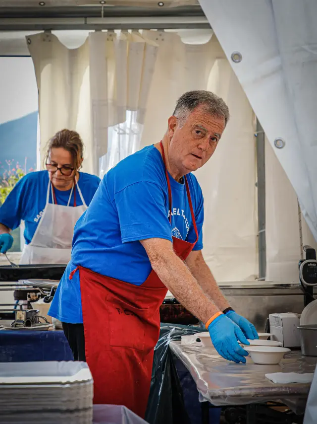 Volontario con grembiule rosso che prepara i piatti nella cucina della sagra
